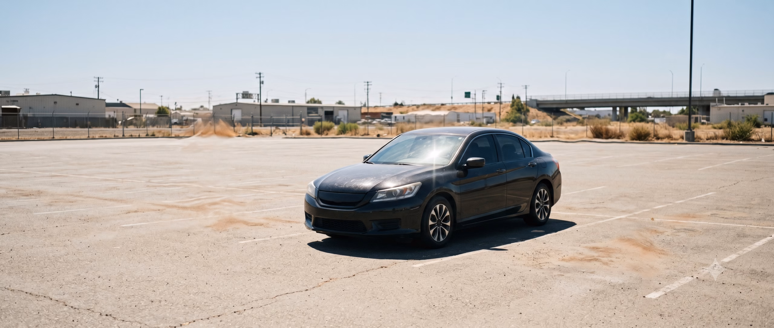 A dark-colored sedan parked in direct midday Sacramento sunlight, faint heat shimmer visible above the hood, the paint surface showing harsh reflections under extreme light.